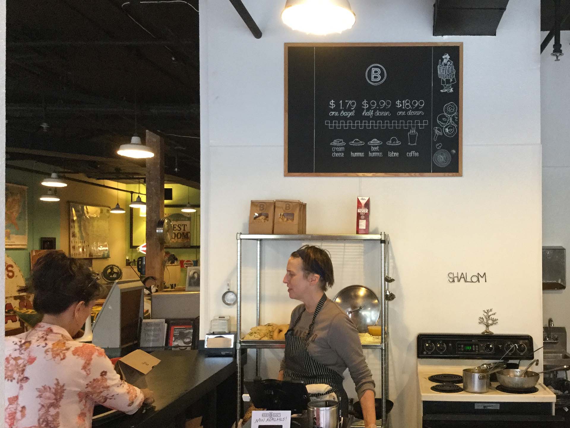 Hand-drawn pricing chalkboard on display behind counter where two women are talking
