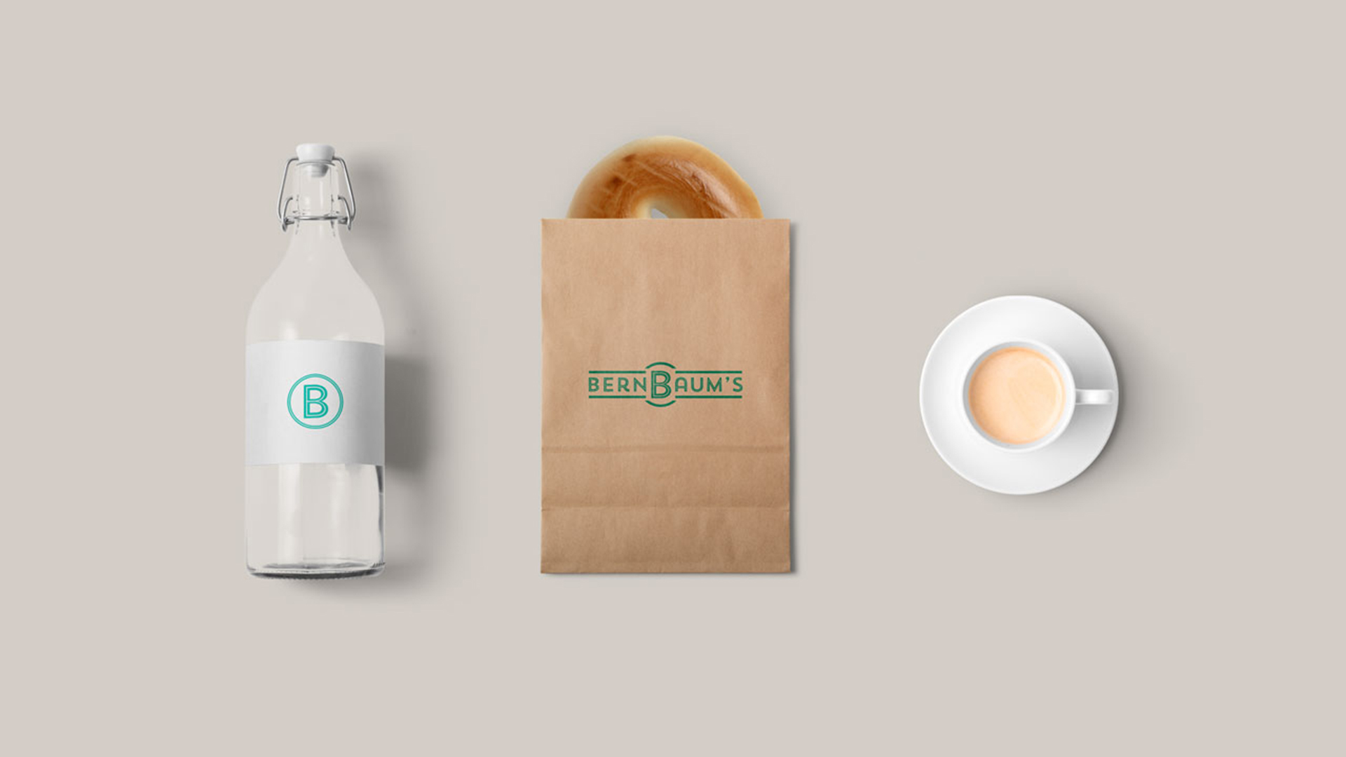 BernBaum's icon printed on water bottle label, logo printed in green on kraft bag with bagel poking out, and cup of coffee