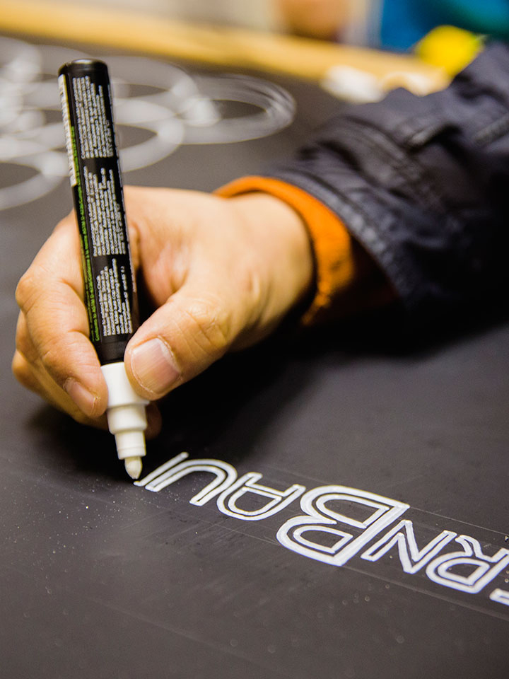 Hand using white chalk marker to paint the BernBaum's logo on a chalk board