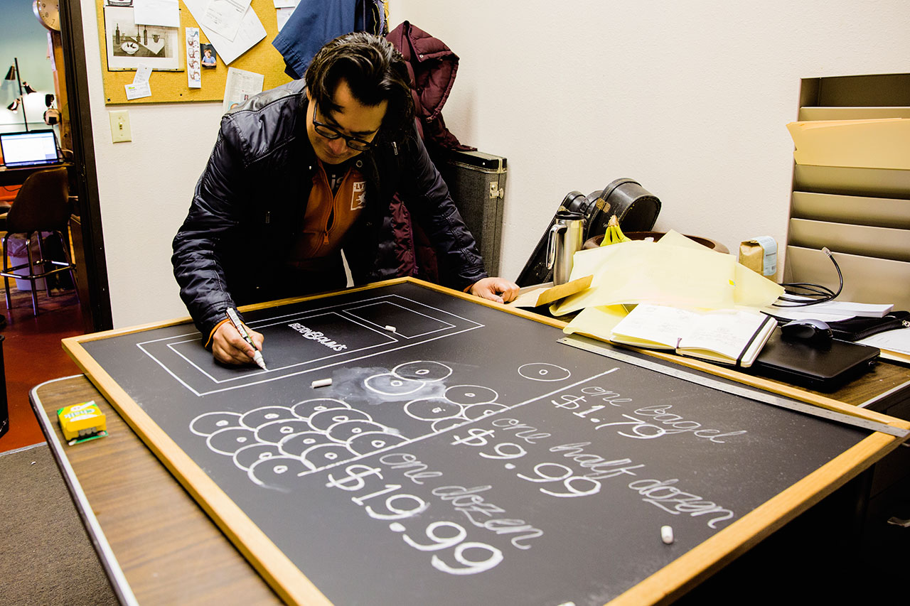 Man drawing prices and bagel illustrations on chalkboard for Bernbaum's