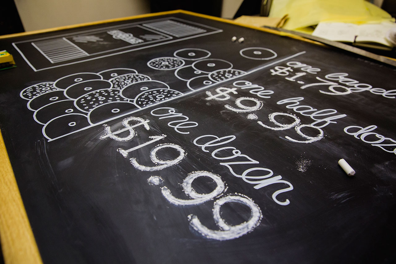 Close-up perspective of pricing and bagels illustrated with chalk on black chalk board