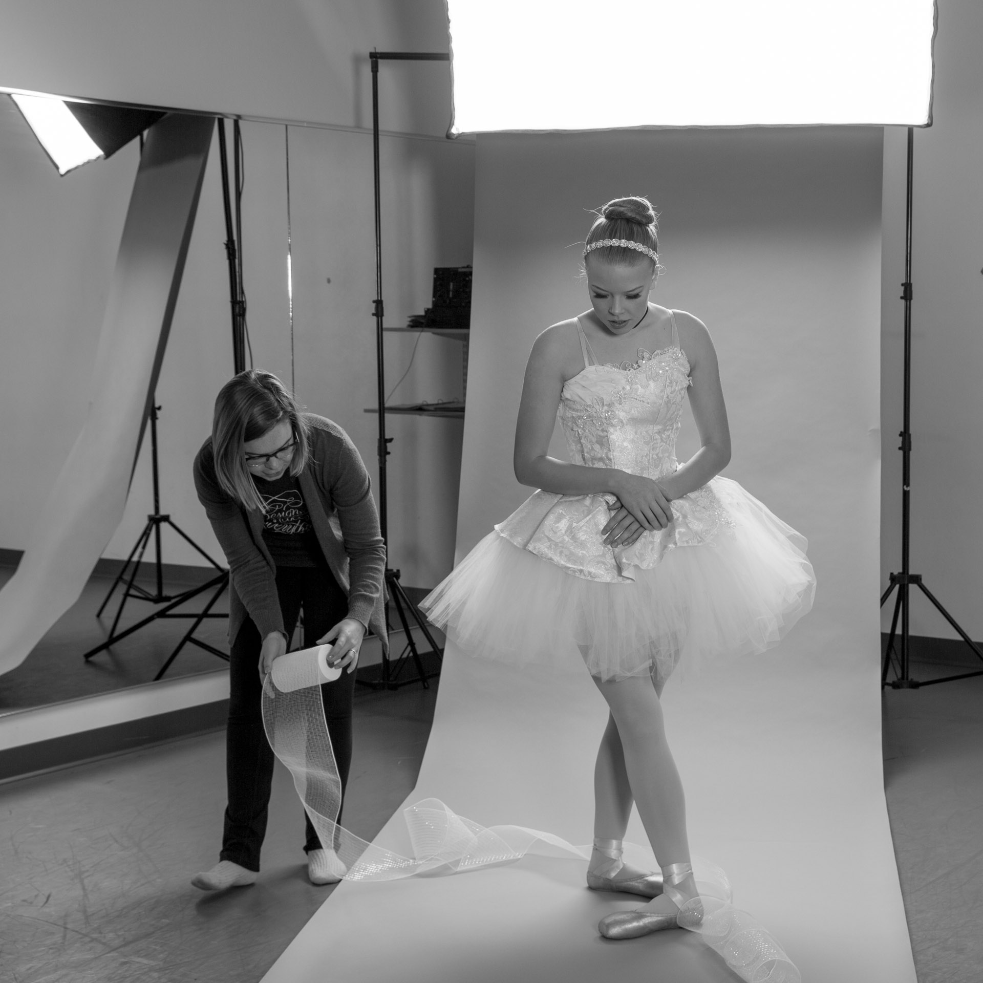 Woman draping tulle around the feet of ballerina dressed in Cinderella tutu in front of photo backdrop