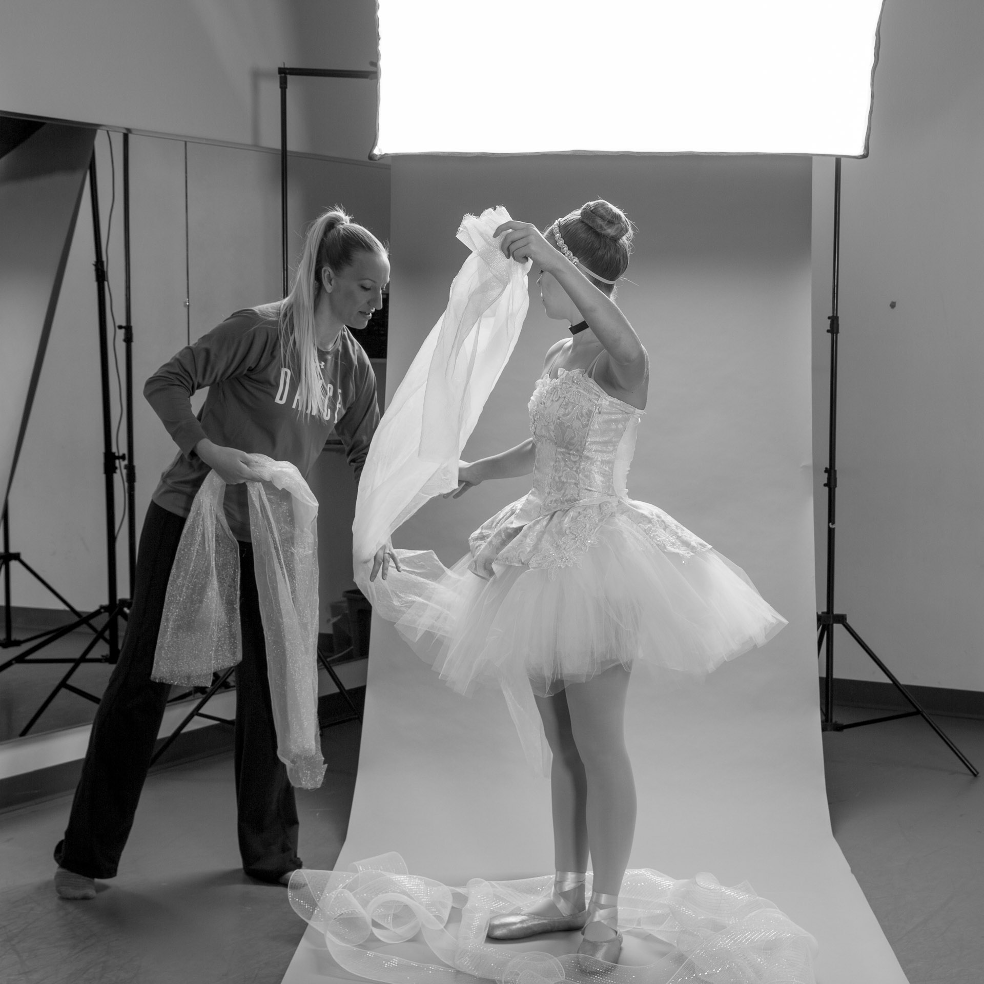 Woman draping tulle and ballerina dressed in Cinderella tutu assisting in front of photo backdrop