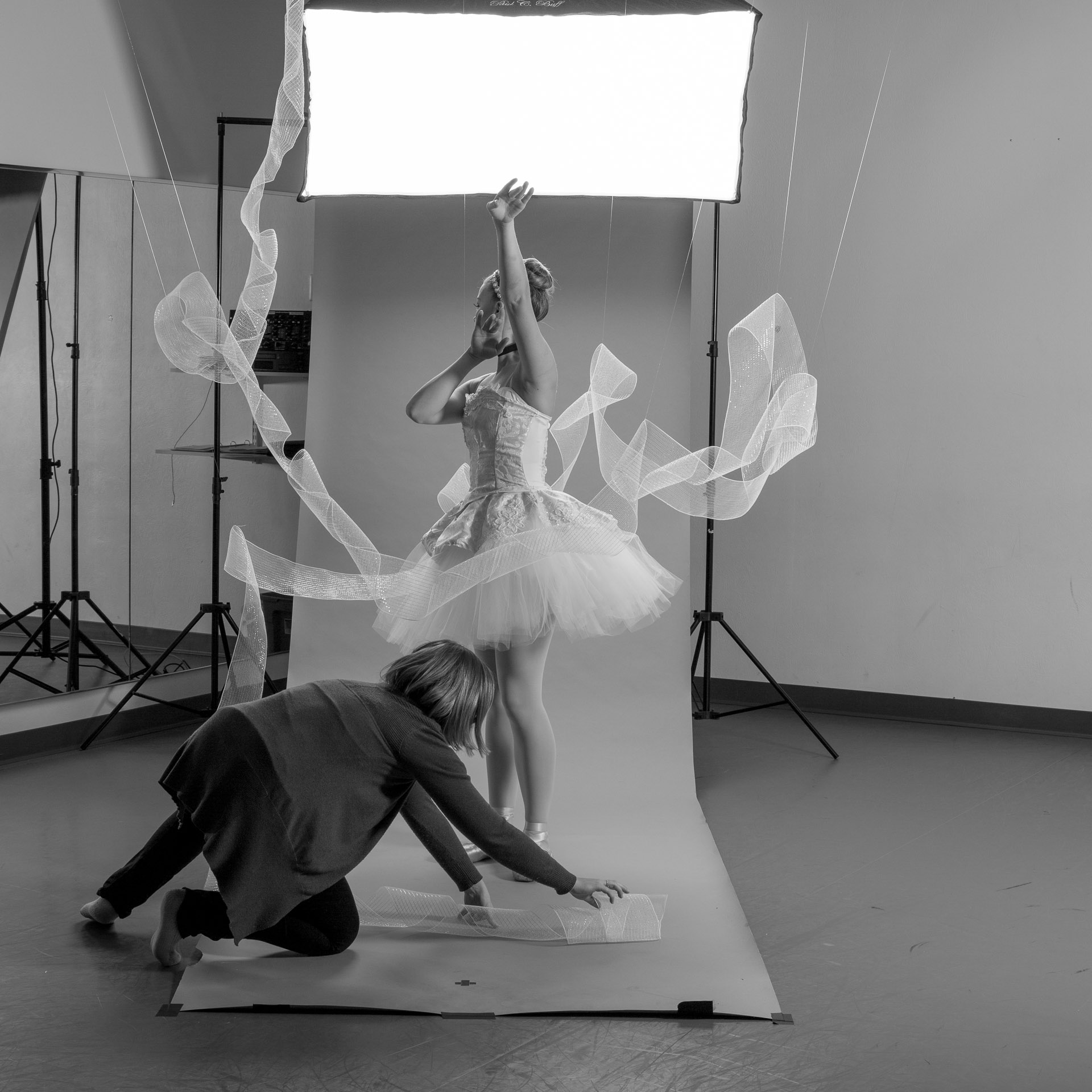 Woman draping tulle around the feet of ballerina dressed in Cinderella tutu in front of photo backdrop