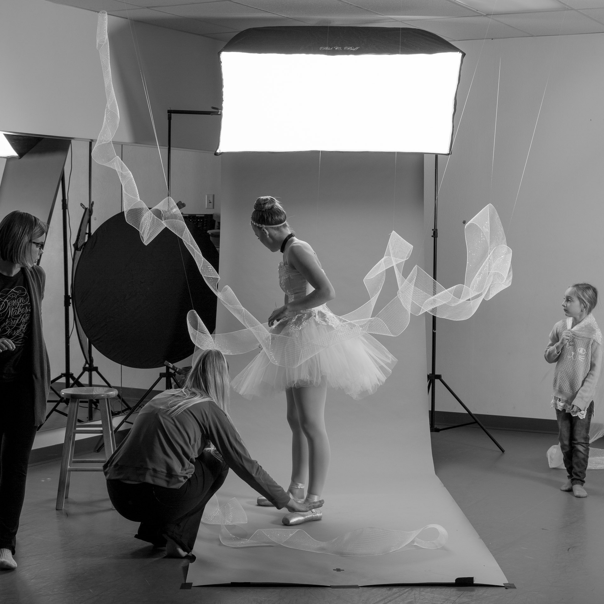 Woman draping tulle around the feet of ballerina dressed in Cinderella tutu in front of photo backdrop