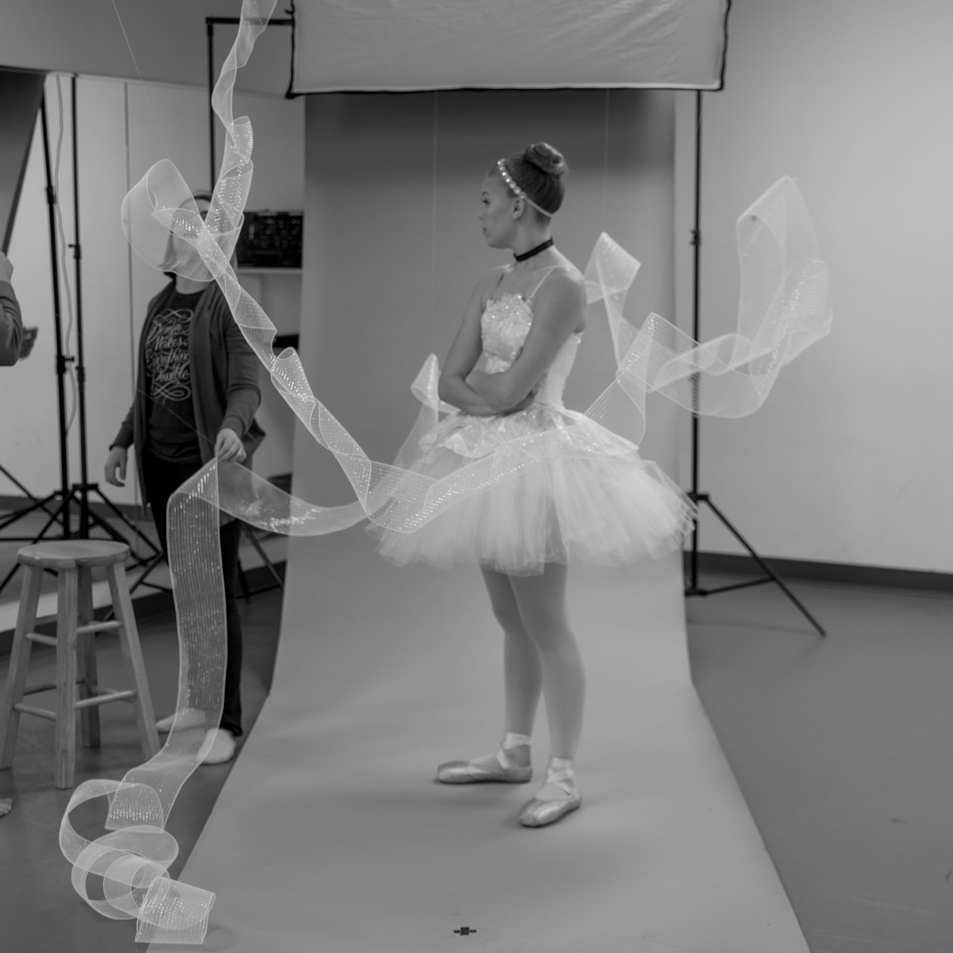 Ballerina dressed in Cinderella tutu in front of photo backdrop while tulle is being draped around her