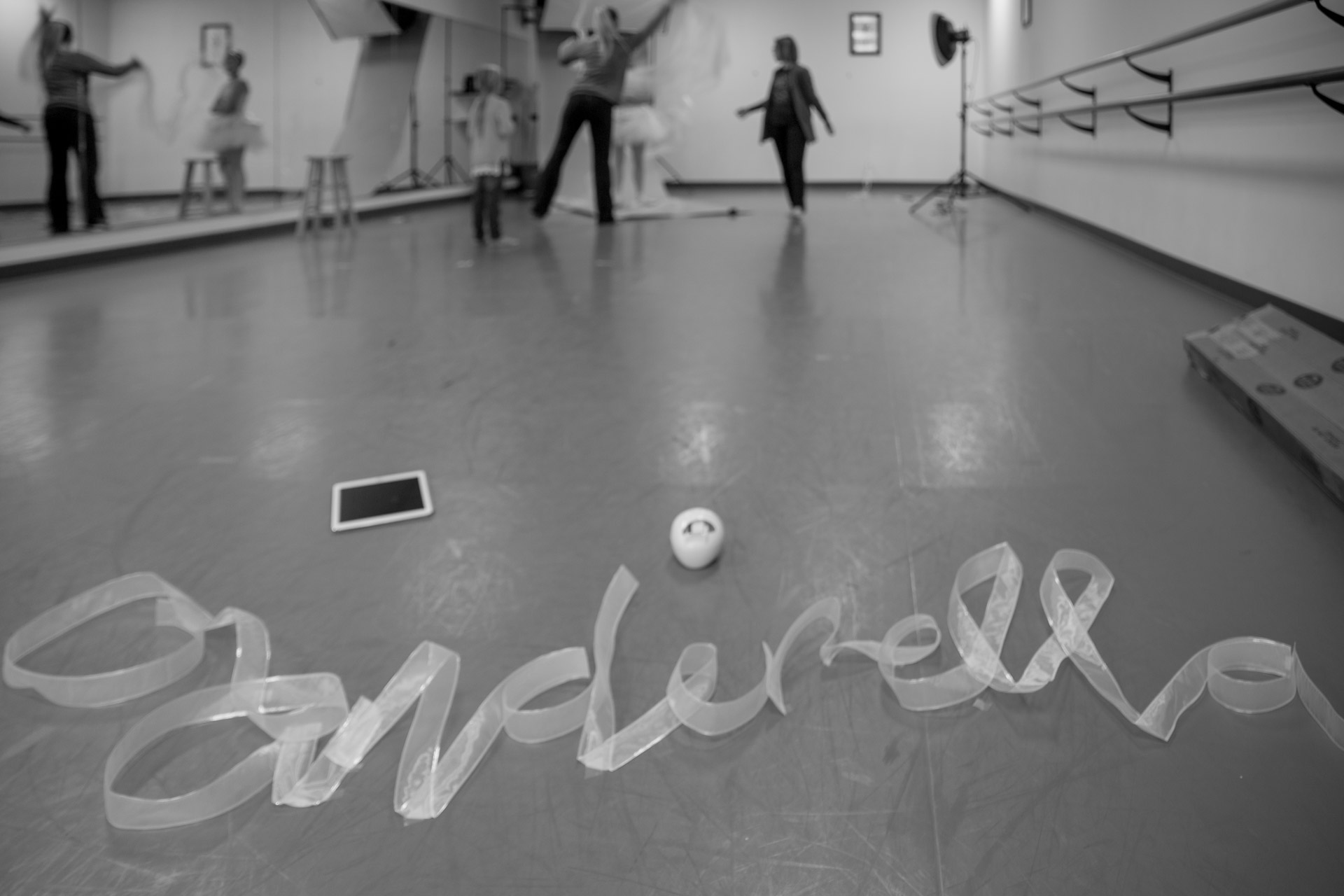 The word Cinderella made from ribbon on floor of dance studio with women in background preparing set