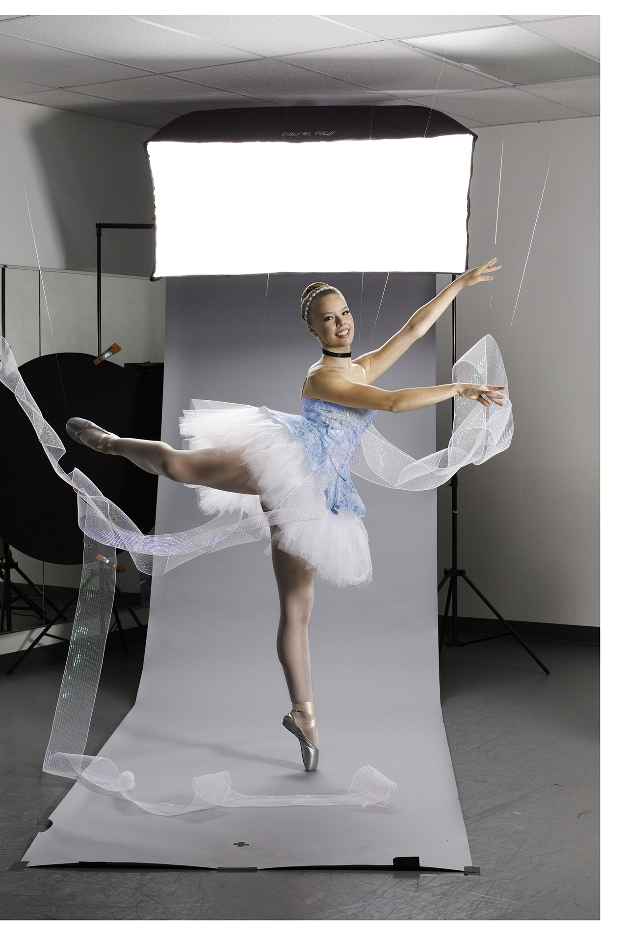 Ballerina dressed in Cinderella tutu poses in front of photo backdrop with tulle draped around her