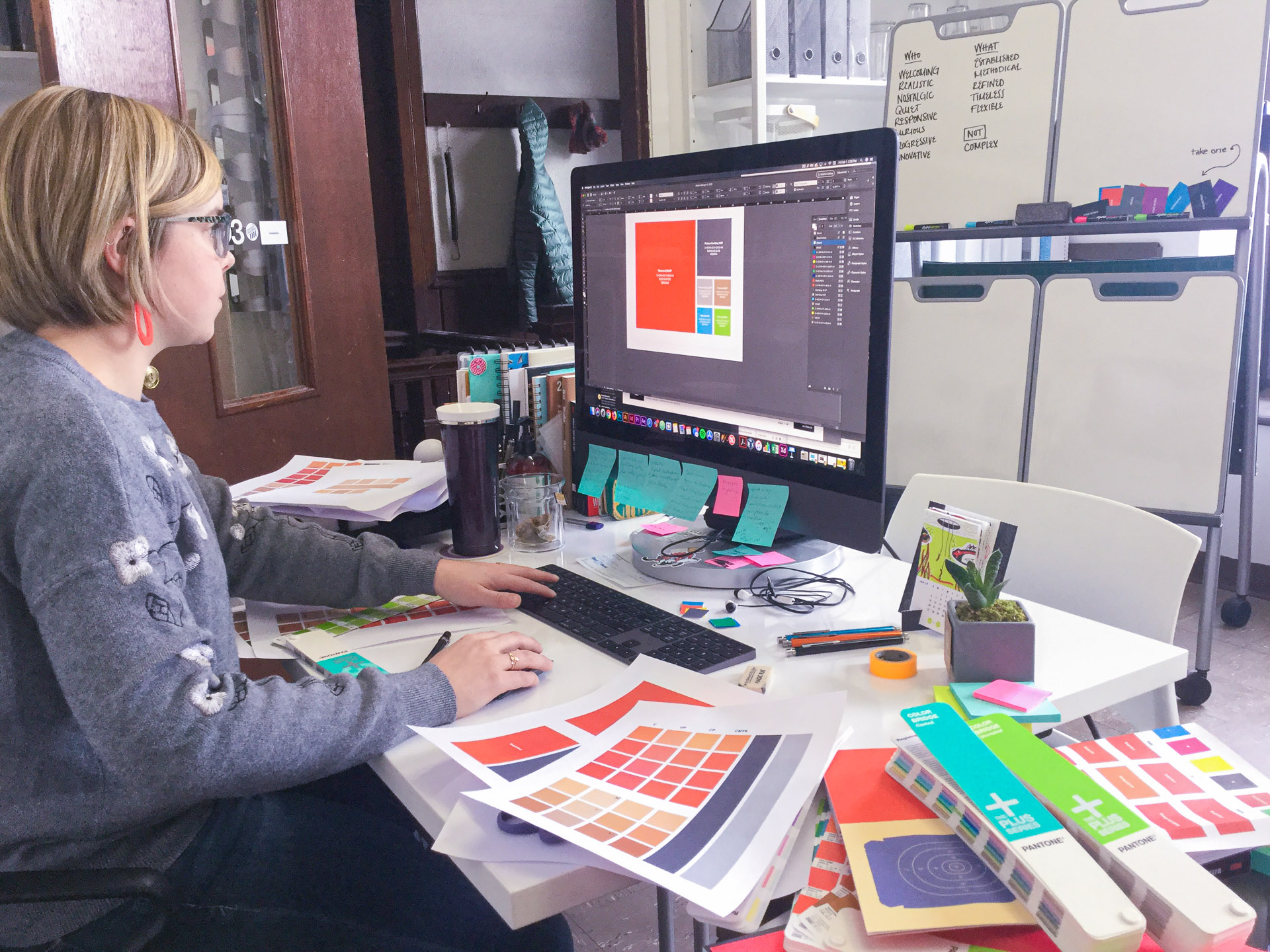 Woman working on the computer looking at the CLLA color scheme on the screen with Pantone color swatch books on her desk