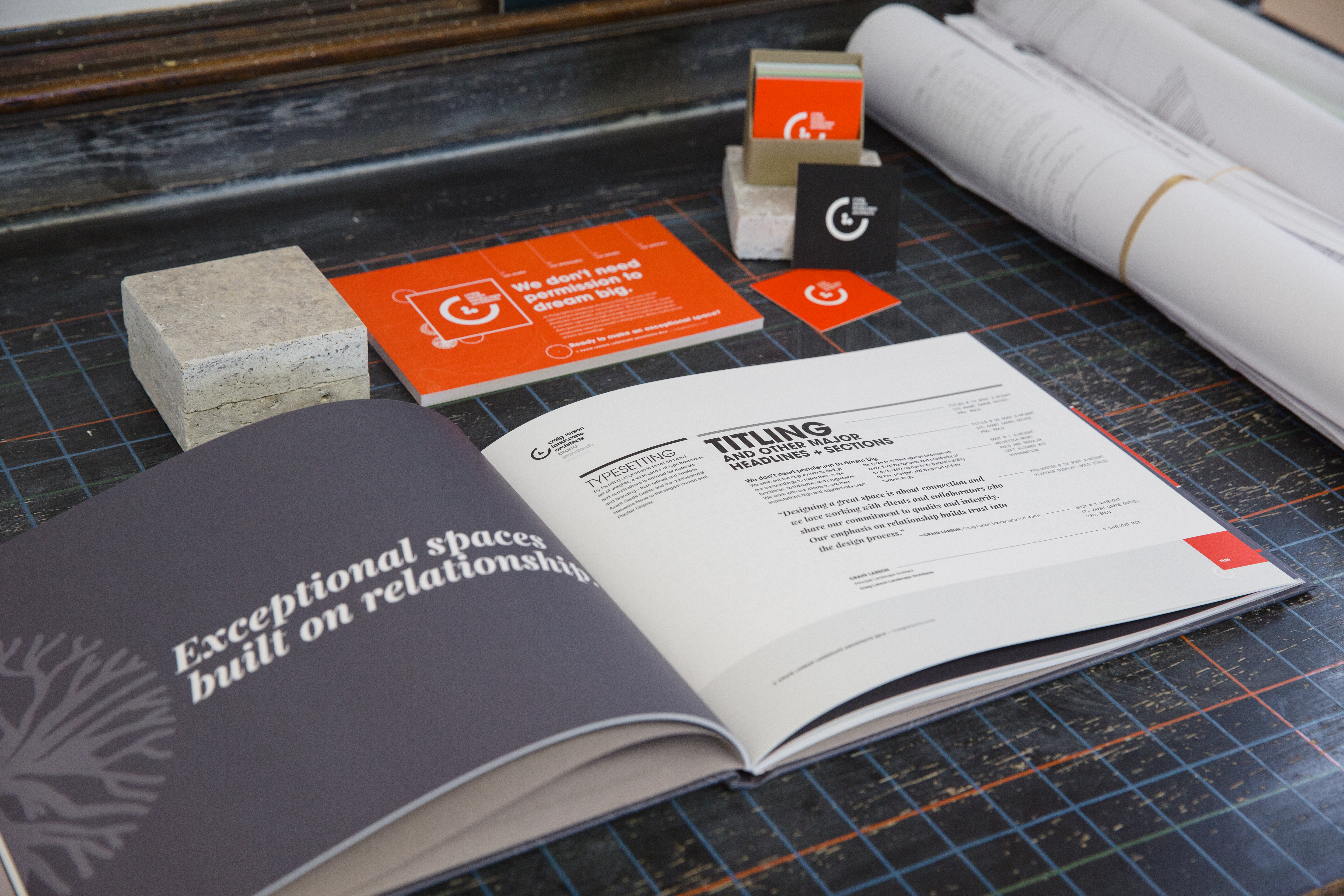 Brand manual displaying typography for CLLA brand identity system next to rolled blueprints on a black gridded mat