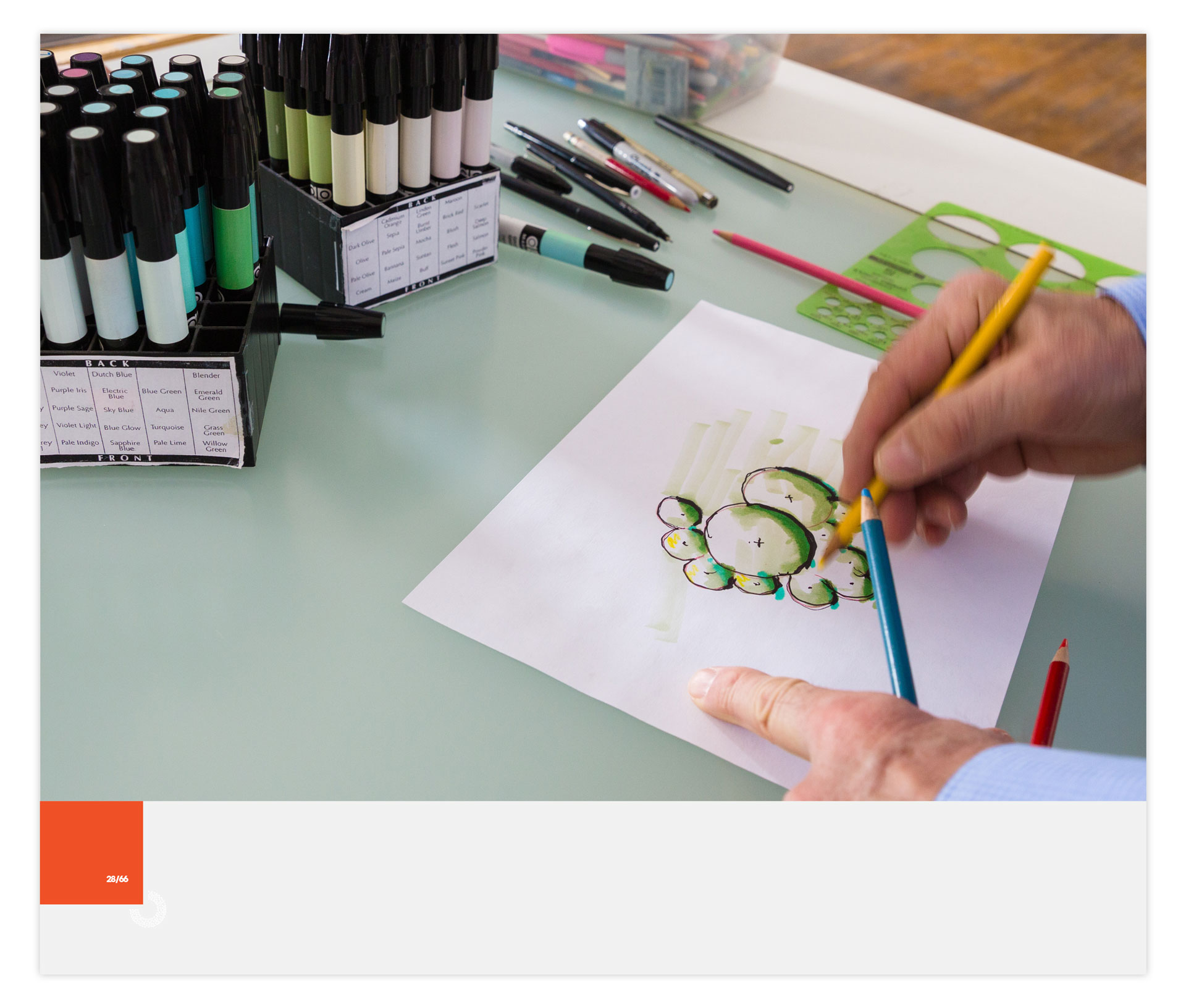 Man's hands drawing shrubs in architectural style and two boxes of markers on the table