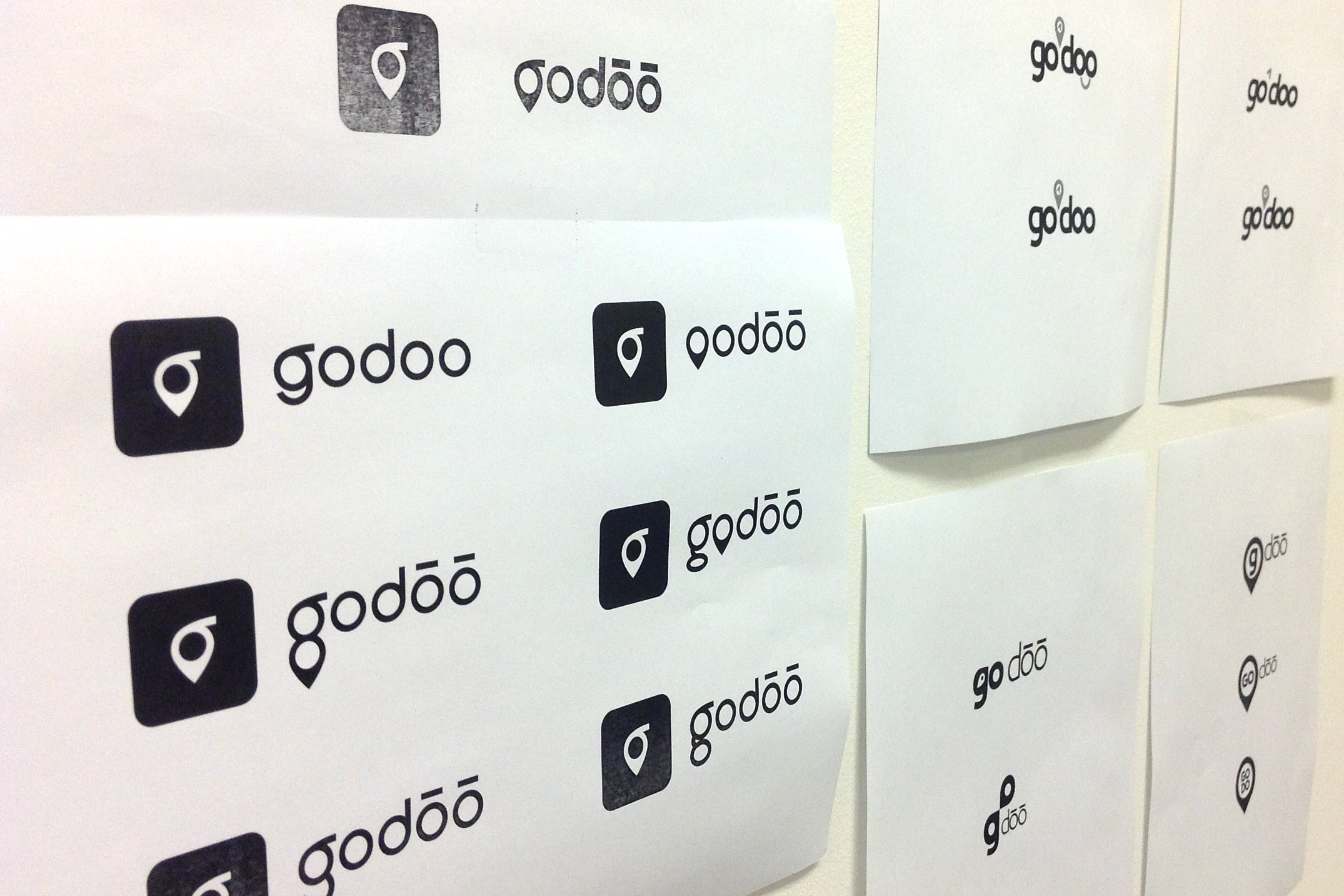 Logo concepts printed on sheets of paper hanging on a white wall