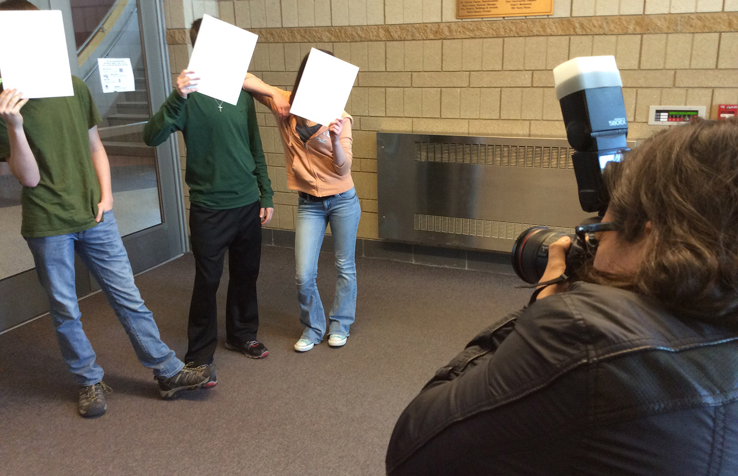 Man taking photo of three kids holding paper over their faces