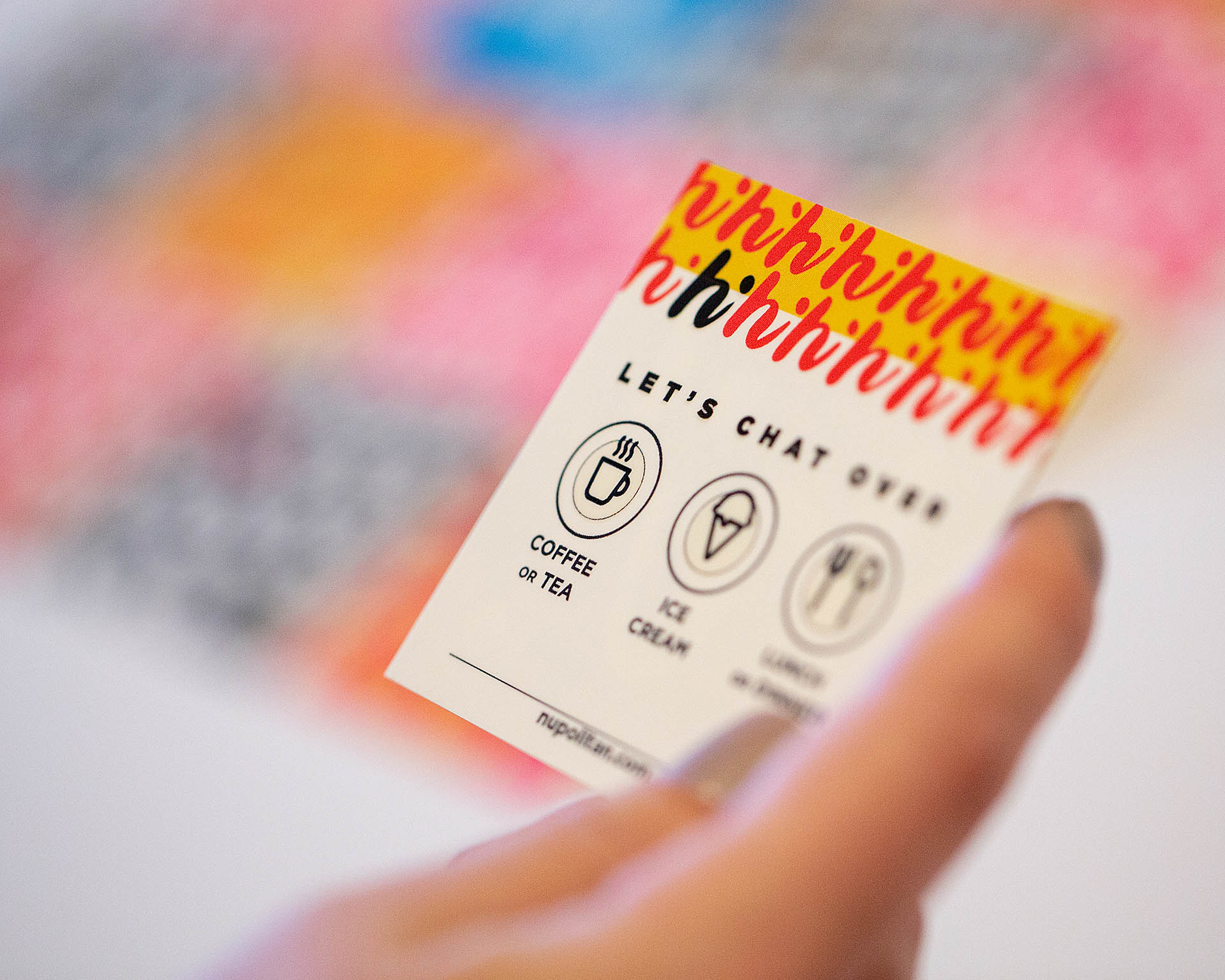 A hand holding a card over a blurred grid of colored, square cards in the background