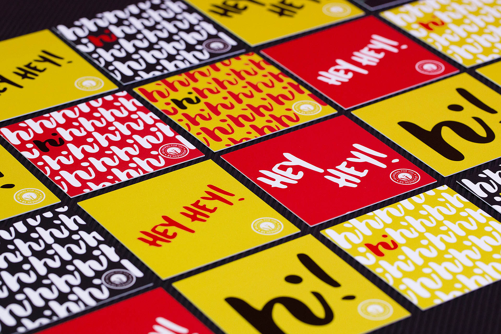 A grid of yellow, red, and black cards with a hi repeating pattern and hey hey printed on them