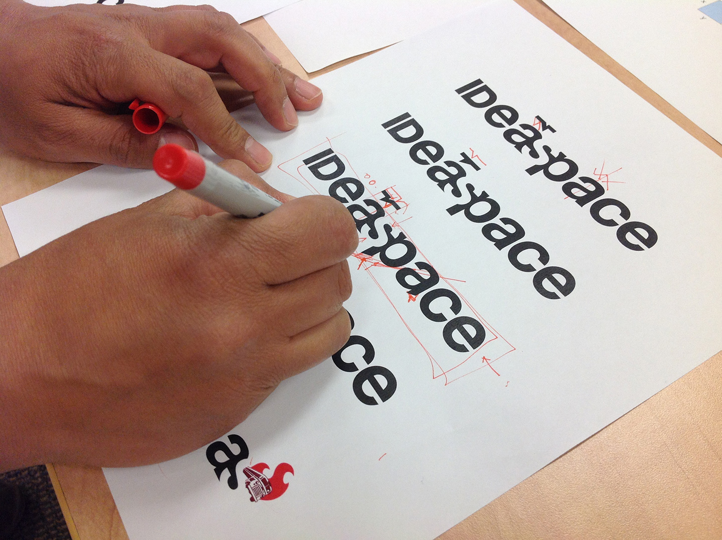 Hands marking up a page featuring IDeaspace logotypes with a red marker