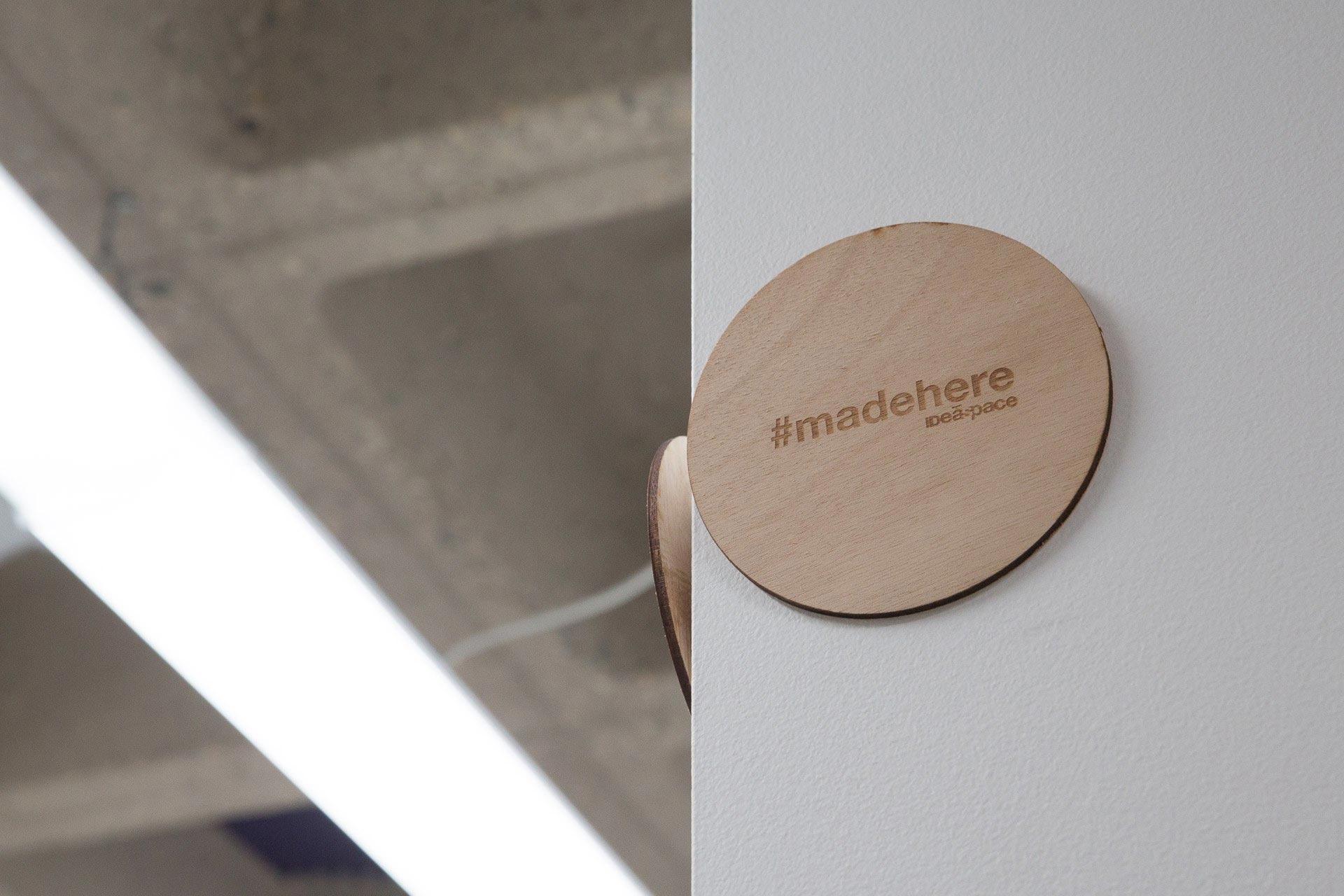 Wooden circle etched with #madehere hanging on the corner of a white wall