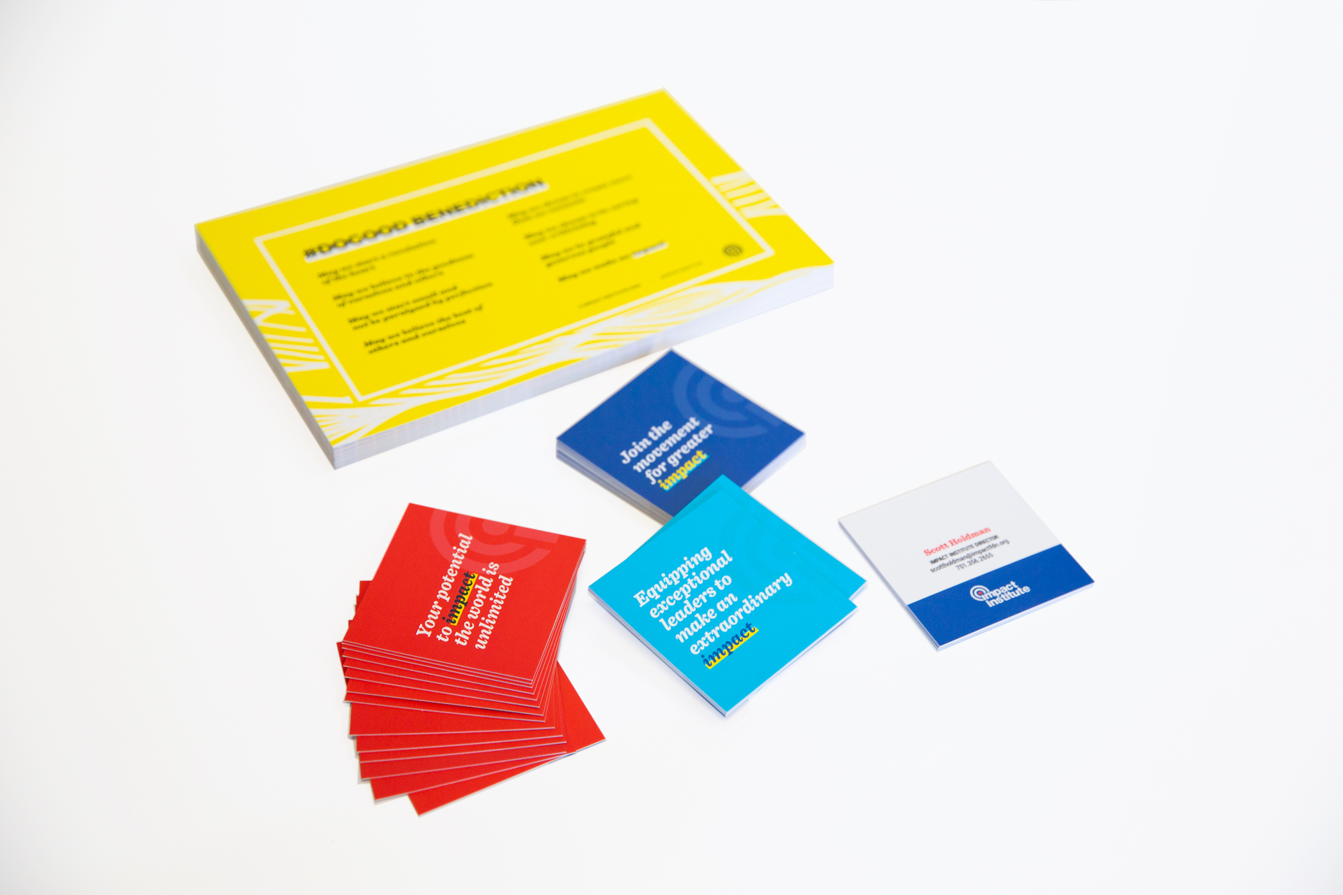 Stack of yellow postcards and scattered red, aqua, and dark blue square business cards on a white surface