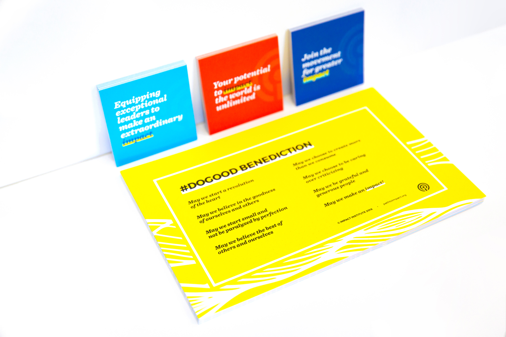 Stack of yellow postcards sitting on and red, aqua, and dark blue square leaning up against a white surface