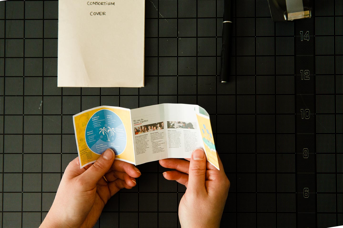 Two hands holding miniature prototype of folded brochure over black gridded background