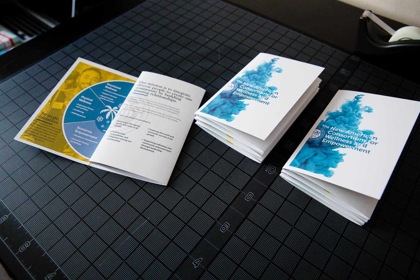 One partially open brochure and two folded brochures on a black gridded background