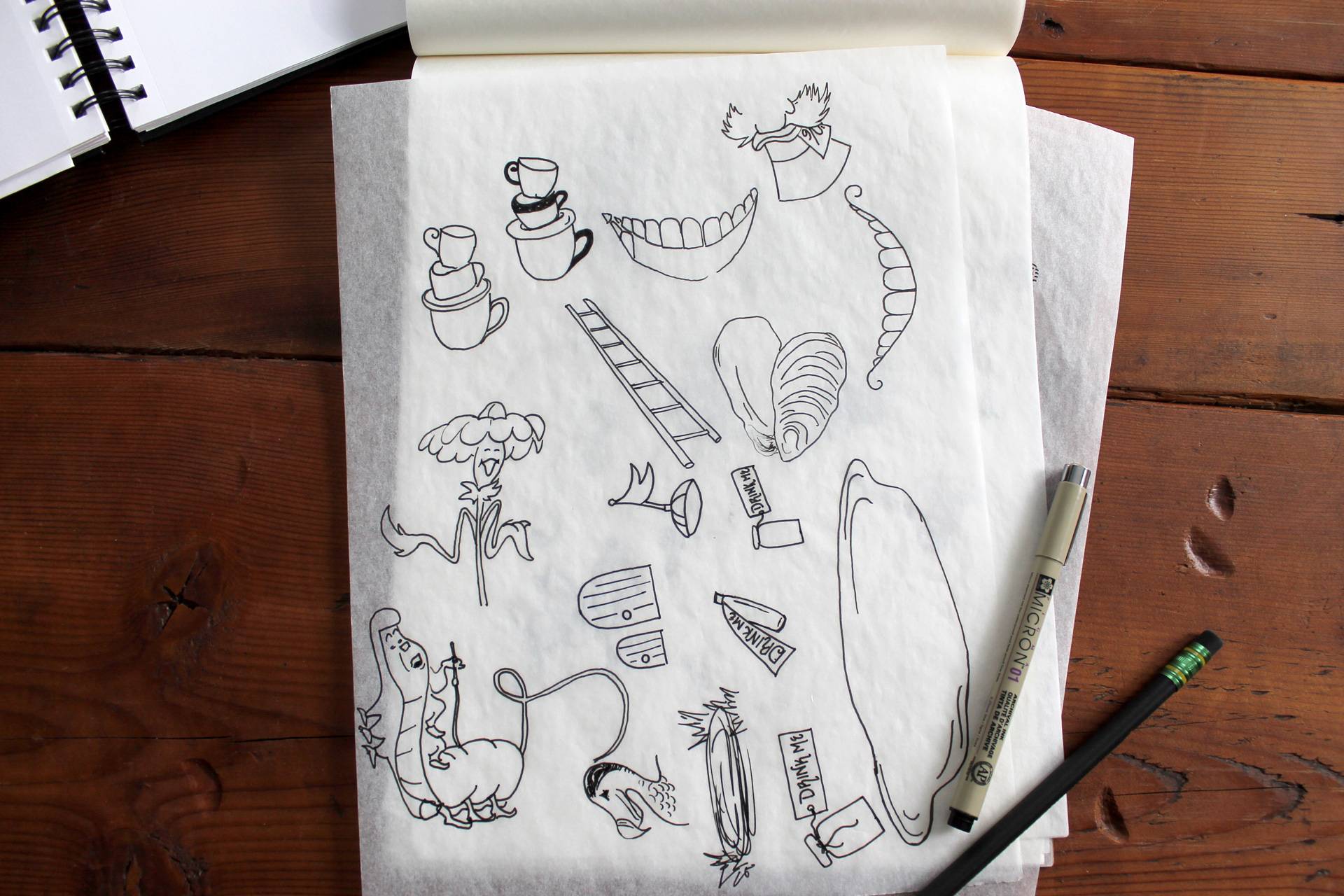 Tracing paper with sketches of animated Alice in Wonderland elements on a wood table next to a pen and pencil