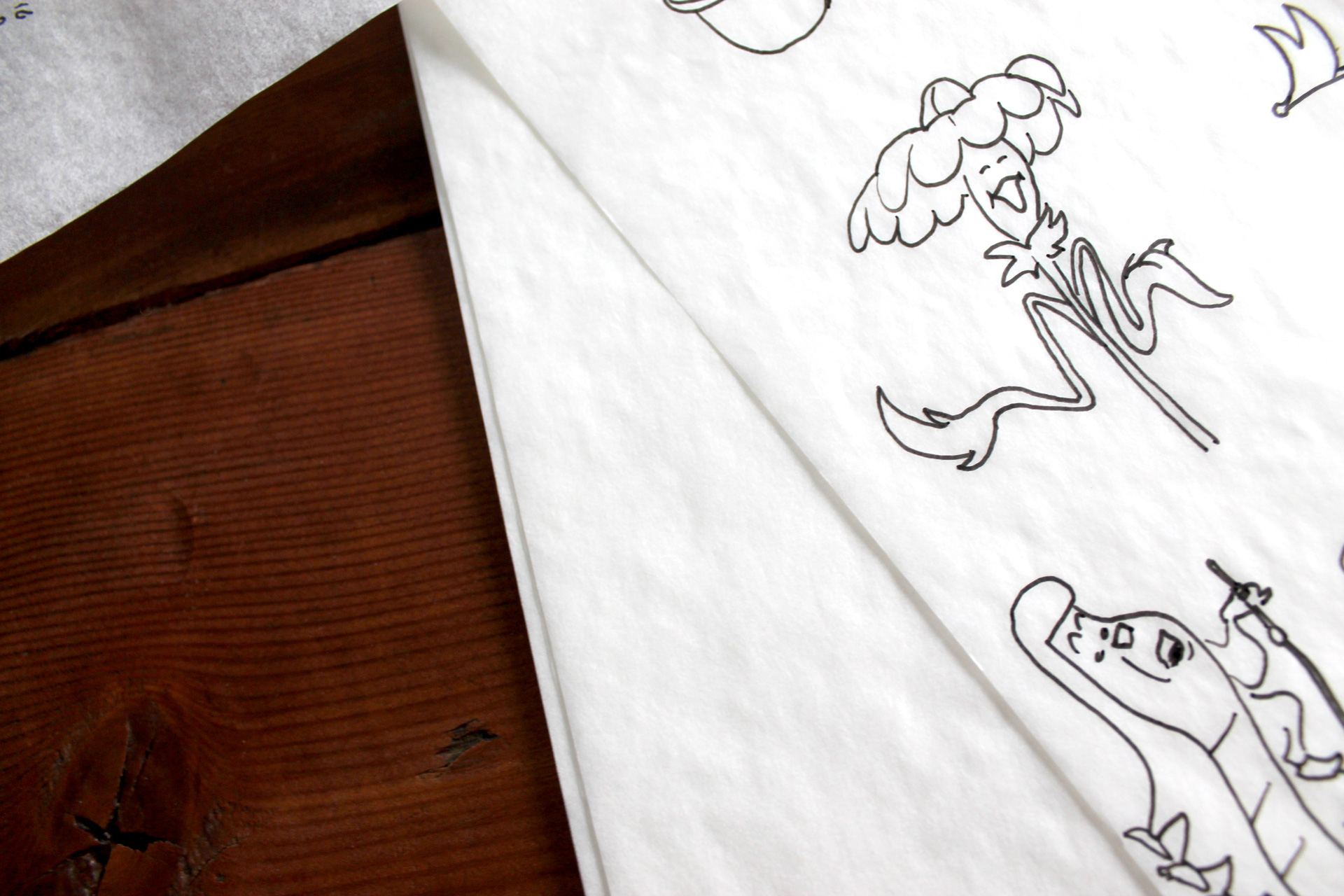 Close up of illustrations on tracing paper sitting on a wooden table