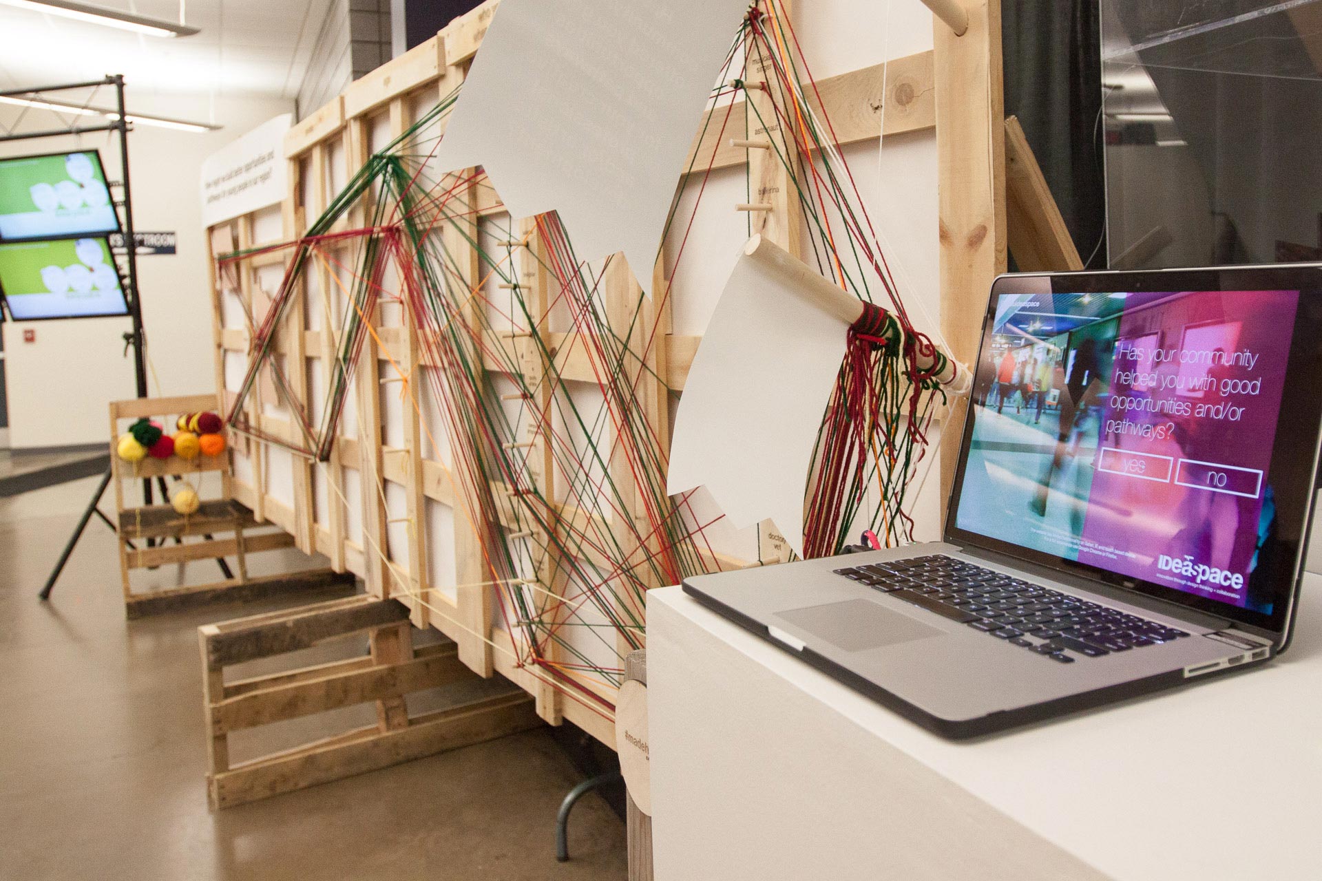 Laptop on white table in front of wood and yarn installation