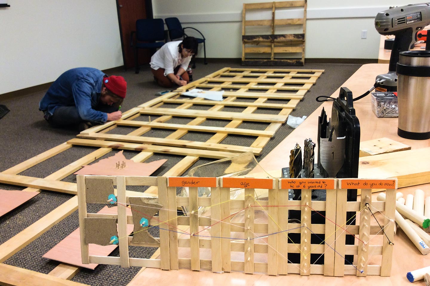 Two people assembling wooden structure with small prototype in the foreground