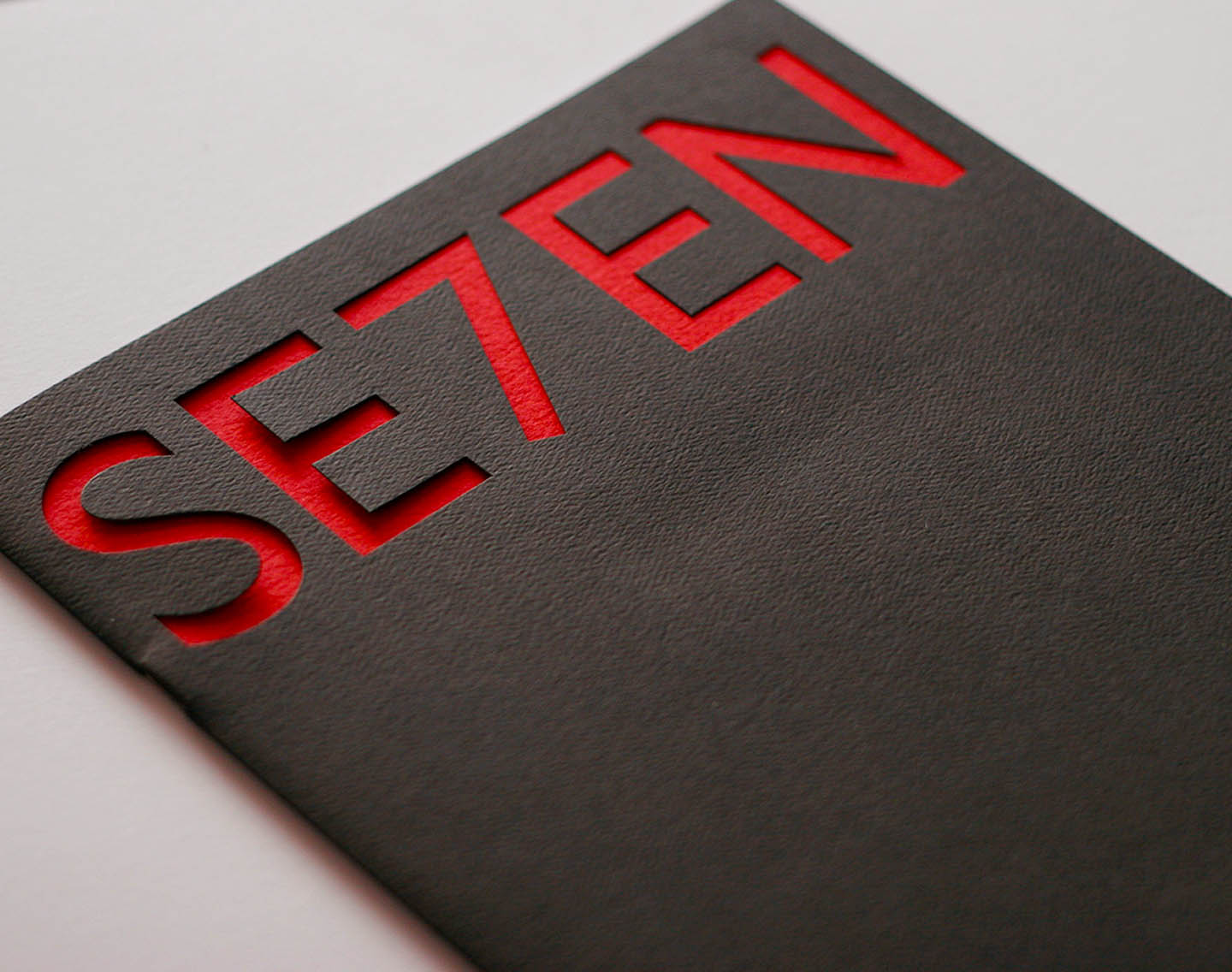 A cutout of the word SE7EN on black cover of magazine with red interior