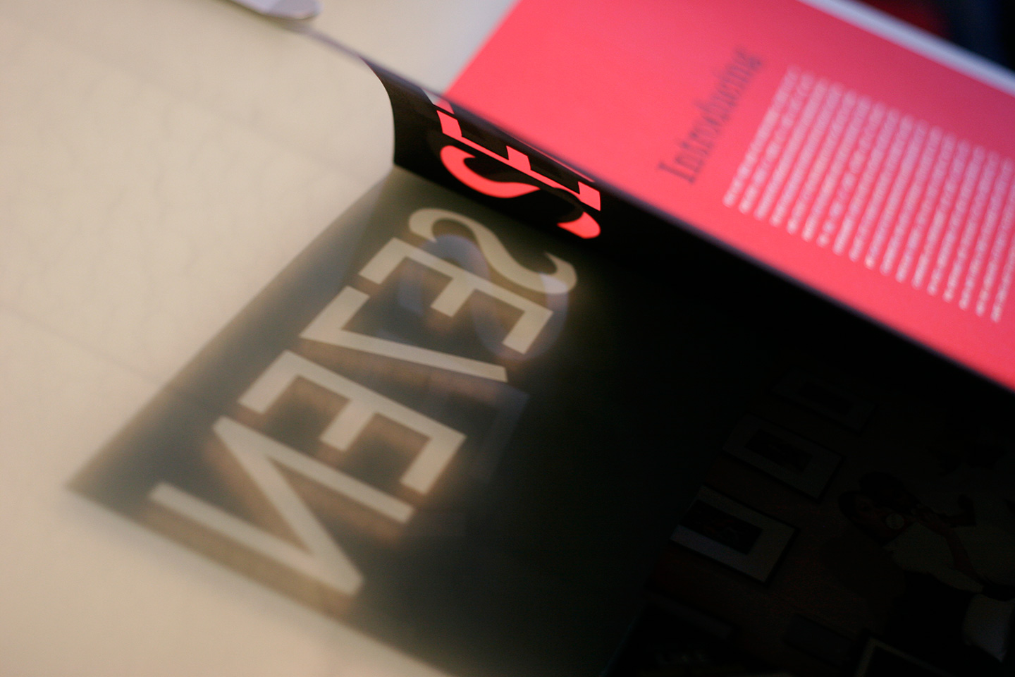 Light reflecting through a cutout of the word SE7EN on black cover of magazine with red interior