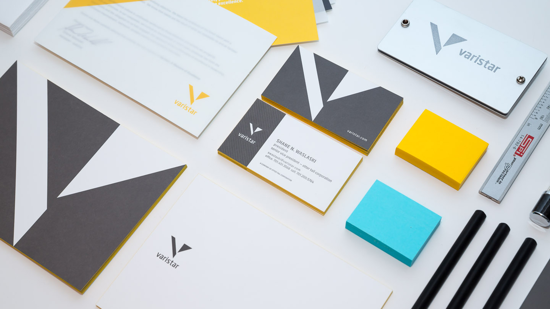 Gray, yellow, and blue letterhead, postcards, business, cards, and colored post-it notes atop a white surface
