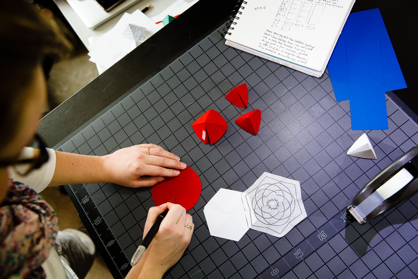 A woman cutting hexagons from red paper with small 3D paper triangles beside her